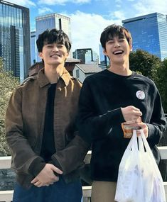 two young men standing next to each other holding bags