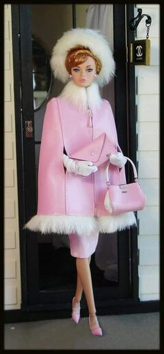 a barbie doll dressed in pink and white holding a handbag while standing next to a door