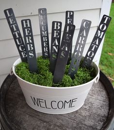 a bucket filled with welcome signs sitting on top of a grass covered table next to a building