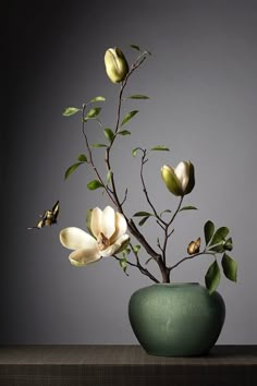 a green vase filled with flowers on top of a wooden table next to a gray wall