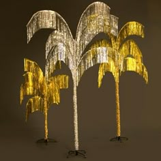 three palm trees made out of gold tinsel and black stand in front of a dark background