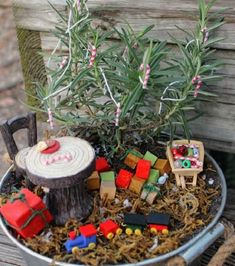 a christmas fairy garden in a metal bucket with toys and decorations on top, sitting on a wooden bench