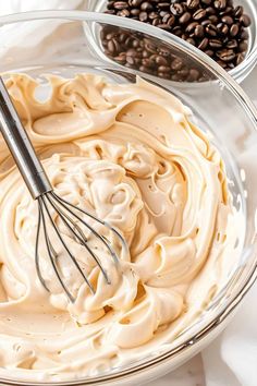 a bowl filled with whipped cream next to coffee beans and a whisk in it