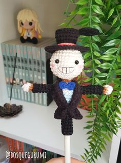 a crocheted doll with a top hat and cane in front of a potted plant