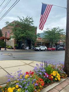 an american flag is flying in the air over a street with flowers and cars on it