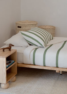 a bed with green and white pillows on top of it next to a night stand