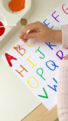 a child's hand is painting letters on a paper