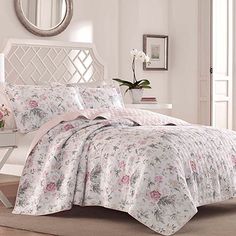 a white bed with pink flowers on it and a mirror in the corner behind it