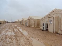 several tents are lined up in the mud on a dirt road with people walking by