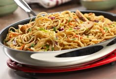 a pan filled with noodles and vegetables on top of a table next to silverware