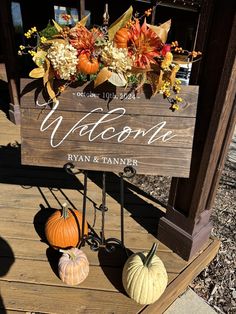 a wooden welcome sign sitting on top of a wooden platform next to pumpkins and flowers