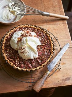 a pecan pie with whipped cream on top sits on a table next to a whisk