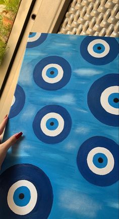 a hand is holding up a piece of art with circles painted on it and blue