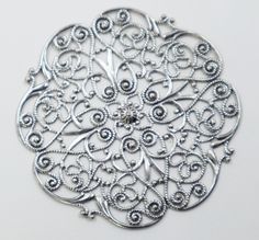 an intricately designed silver brooch sits on a white surface, surrounded by filigrees and beads