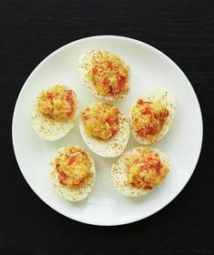 small deviled eggs on a white plate topped with cheese and tomato sauce, ready to be eaten