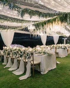 an outdoor wedding setup with white linens, greenery and lights hanging from the ceiling