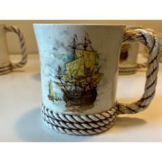 two mugs with rope handles and designs on them sitting on a white counter top