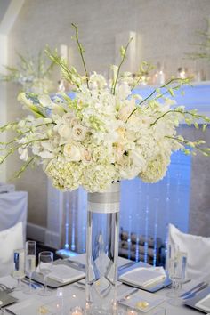 a vase with white flowers sitting on top of a table next to plates and silverware