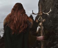 a woman with long red hair standing next to the ocean and looking at an antelope