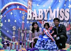 two adults and a child posing for a photo in front of the baby miss trophy