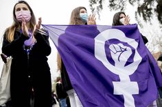 two women wearing face masks and holding a purple flag with the symbol of female power