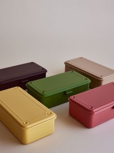 four different colored lunch boxes sitting next to each other on top of a white surface