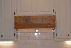 a kitchen with white cupboards and tile backsplash, lights above the sink