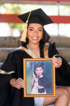 a woman in graduation cap and gown holding up a framed photo with the graduate's name on it