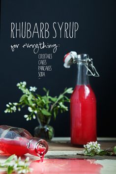 a bottle of rhubarb syrup next to a vase with flowers