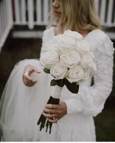 a woman holding a bouquet of white roses in her hand and wearing a wedding dress