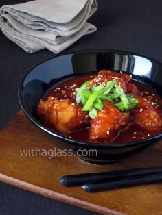 a black bowl filled with meat and vegetables on top of a wooden cutting board next to chopsticks