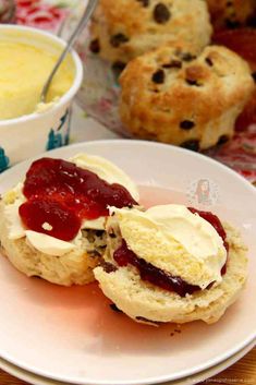 scones filled with jam and cream on a plate next to bowls of buttery biscuits