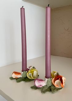 two purple candles with flowers on them sitting on a table next to another candle holder