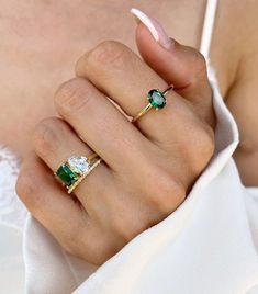 a woman's hand with two rings on her finger and an emerald ring in the middle