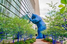 a large blue bear statue sitting in the middle of a garden next to a tall building