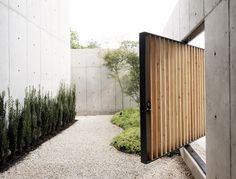 a wooden door is open in front of a concrete wall and gravel area with plants