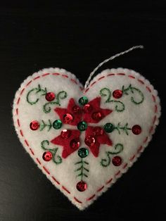 a heart shaped ornament decorated with red and green sequins on a black surface