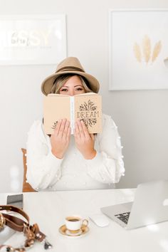 a woman sitting at a table with a book covering her face