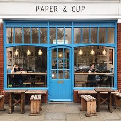 a woman sitting on a bench in front of a blue door with the words paper and cup