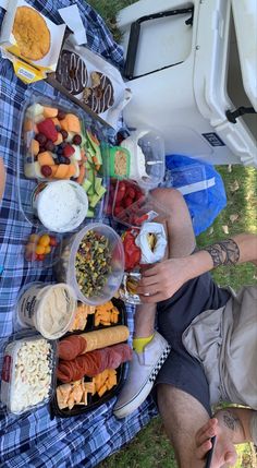 a man sitting in the grass with food and drinks on his lap next to him