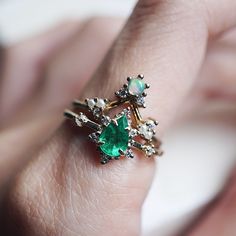 a woman's hand holding an emerald and diamond ring