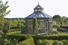 a gazebo in the middle of a garden surrounded by hedges and trees with flowers