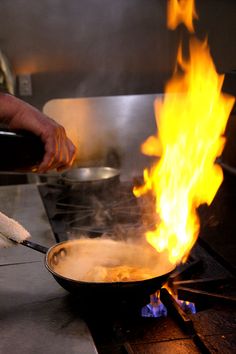 a person cooking food on top of a stove with flames coming out of the pan