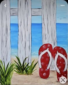 a pair of red flip flops sitting on top of a sandy beach next to the ocean