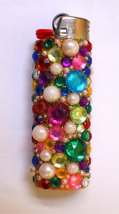 a cell phone covered in lots of different colored stones and pearls on a white surface