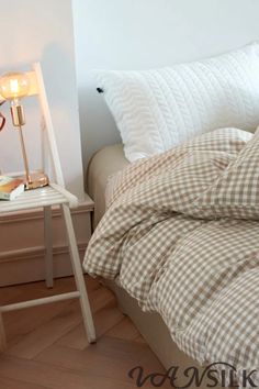 a bed with two pillows on top of it next to a night stand and lamp