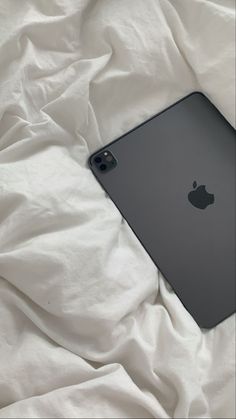 an apple ipad is laying on a bed with white sheets and blankets behind it,