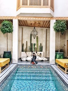 a woman sitting on a couch next to a swimming pool with yellow chairs around it