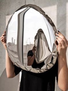 a woman holding up a large mirror to her face