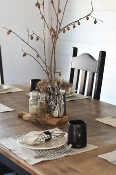 a wooden table topped with a vase filled with flowers next to plates and utensils